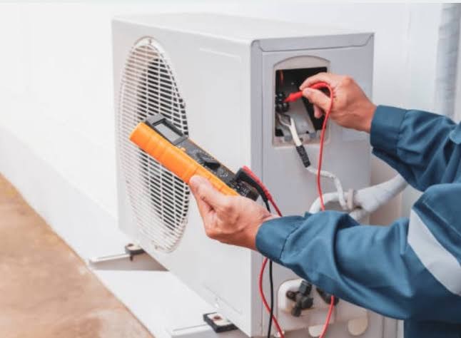 Technician testing electrical connections on an outdoor heat pump